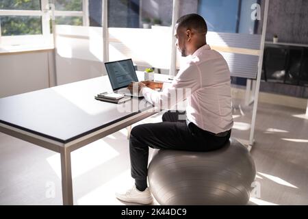 Correct Posture At Desk In Office Using Fitness Ball Stock Photo