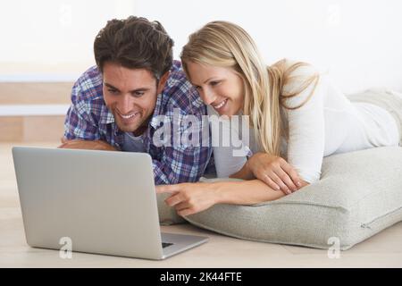 The world at their finger tips. A happy young couple lying on the floor at home and using a laptop together. Stock Photo