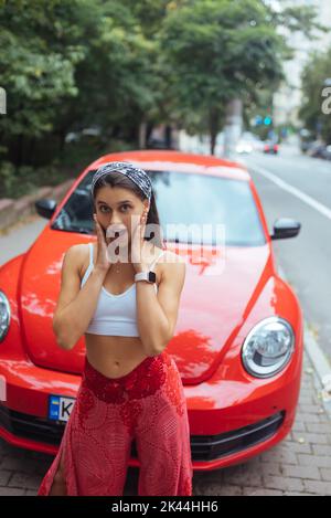 Portrait of pretty Caucasian woman standing against new red car Stock Photo