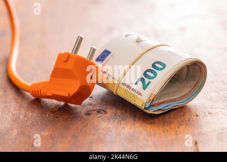Electric plug and the euro money on wooden table. Concept of increasing electric prices. Stock Photo