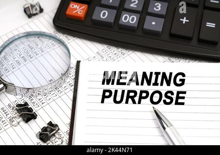 Business concept. On the table is a magnifying glass, a calculator, a pen and a notebook with the inscription - Meaning Purpose Stock Photo