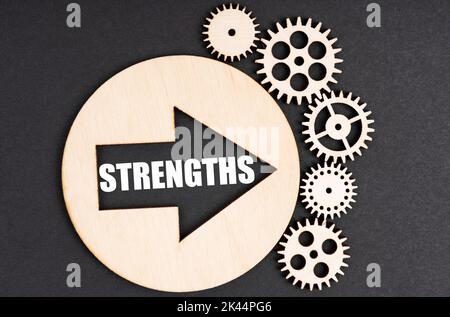 Business and finance concept. On a black background, there are wooden gears and a circle inside which there is an arrow with the inscription - STRENGT Stock Photo