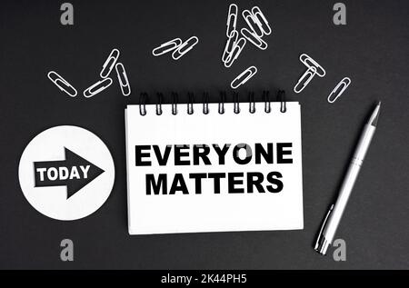 Business concept. On a black background, a round plate - Today and a notebook with the inscription - Everyone Matters Stock Photo