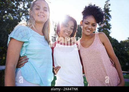 We will always be there for each other. Portrait of three young friends standing in a park with arms around each other. Stock Photo
