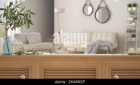 Wooden table top, cabinet, panel or shelf with shutters close up. Olive branch in vase and candles. Blurred background with white living room with sof Stock Photo