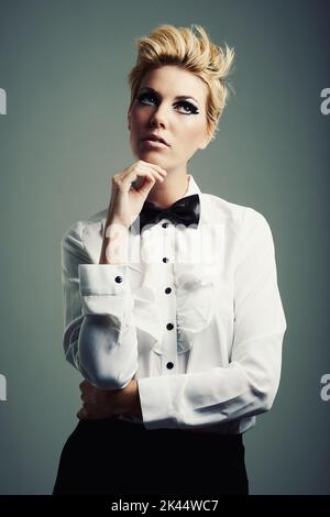 Well, thats a thinker. Studio shot of a beautiful young woman wearing a shirt and bow tie against a gray background. Stock Photo