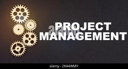 Business and industry concept. On a black background, gears and the inscription - PROJECT MANAGEMENT Stock Photo