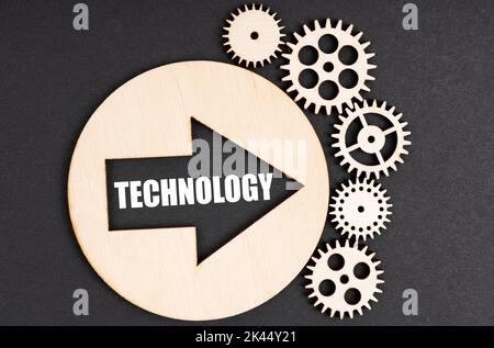 Business and finance concept. On a black background, there are wooden gears and a circle inside which there is an arrow with the inscription - TECHNOL Stock Photo
