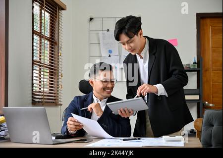 Successful and smart Asian businessman working in the office, checking his meeting schedule on the tablet with his young assistant. Stock Photo