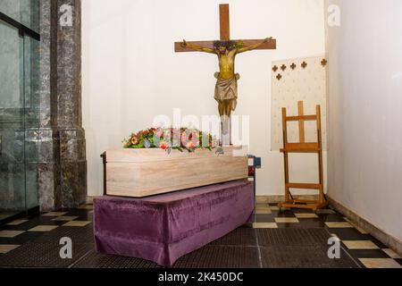 coffin with flowers on it in church with Jezus Christ against the wall waiting to be transported for the service Stock Photo