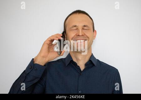 a handsome man in a shirt is talking on the phone and laughing on a white background Stock Photo