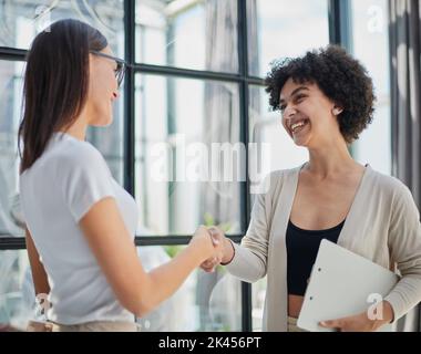 Two Businesswomen Shaking Hands In Modern Office Stock Photo