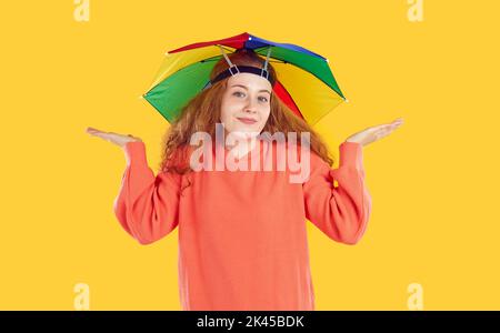 Portrait of happy clueless young woman in funny umbrella hat shrugging her shoulders Stock Photo