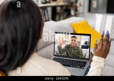 African woman using laptop for video connection with male friend or coworker, multiracial lady talking via video call with handsome man, girlfriend chatting online with boyfriend on the distance Stock Photo