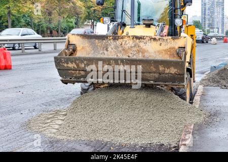 Yellow skid steer wheel loader loading and unloading sand gravel mix on road repair. The concept of construction and repair. Stock Photo