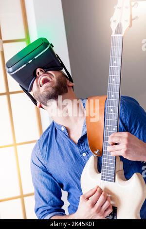 young adult playing guitar at home using viewer for virtual reality Stock Photo