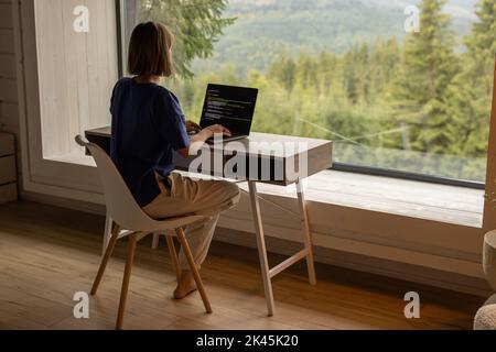 Woman works on laptop remotely in house on nature Stock Photo