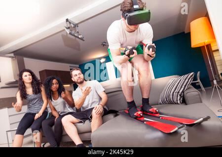 group of friends having fun at home skiing using viewer for virtual reality Stock Photo