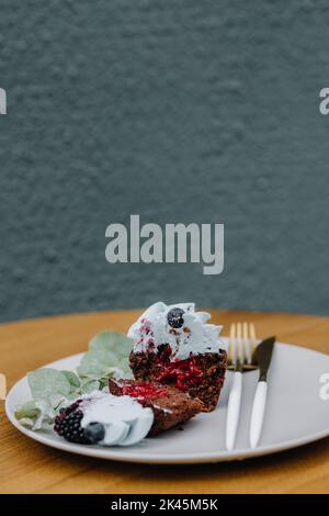 Photo of cut cupcake with utensils on table with berries on white plate. Vertical photo Stock Photo