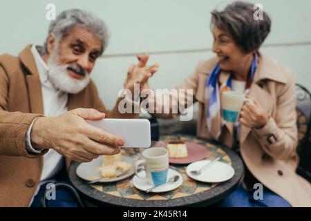 blurred and happy senior couple having video call during breakfast on terrace of cafe,stock image Stock Photo