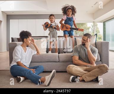 Stress, family and energy with kids playing music on a guitar in the living room at home while giving mom and dad a headache. Mental health, children Stock Photo