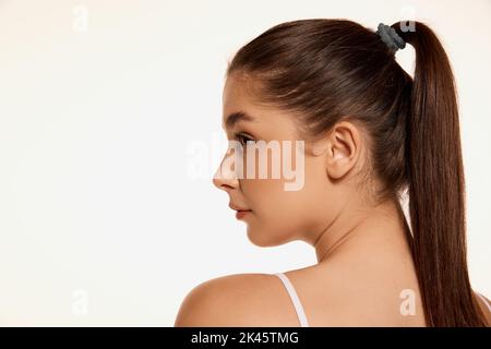 Portrait of young beautiful woman with clear spotless skin and long shiny hair isolated over white background. Side view Stock Photo