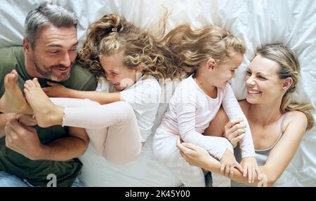 Happy, family and children with a smile in a home bedroom bed spending quality time together. Young girl kids, mother and man at a house with Stock Photo