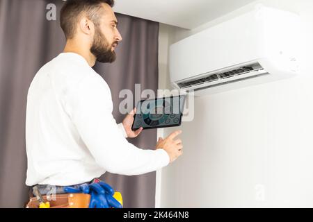 male technician service worker diagnosing for repairs air conditioner. person using tablet. Stock Photo