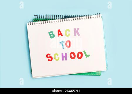 Back to school write in a notebook with colored toy wooden letters on a light blue background Stock Photo