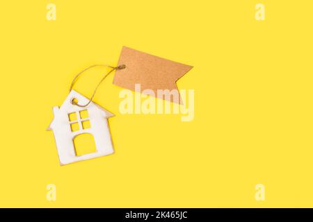 A cardboard house with a brown blank paper label on a yellow background with copy space Stock Photo