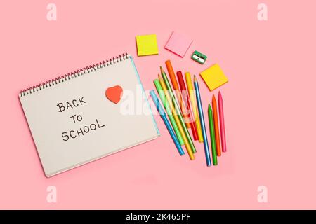 Back to school write in a notebook, colored pencils and markers on a pink background with copy space Stock Photo