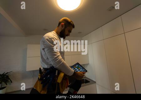 Installation lighting. Builder is holding a tablet in his hands. Concept - lighting engineer. Process installing. Electrician Stock Photo