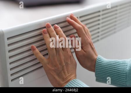 Woman's hand on a white radiator. Heating season. Energy crisis. Cold batteries. Central heating Stock Photo