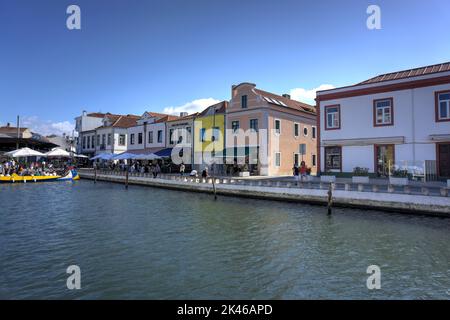 Aveiro, Portugal - August 14, 2022: Canal Do Cojo with waterside cafes, motion blurred pedestrians and gondola loading with tourists Stock Photo