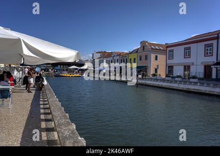 Aveiro, Portugal - August 14, 2022: Canal Do Cojo with waterside cafes, motion blurred pedestrians and gondola loading with tourists Stock Photo