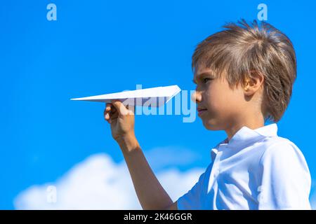 Child throwing white paper plane. Boy playing with paper airplane against blue sky on sunny day outdoors Stock Photo