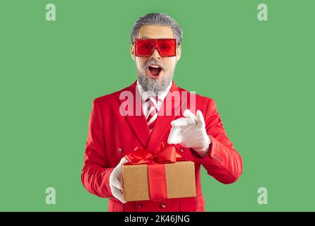 Wondered cheerful old man showman wearing in Santa style holding Christmas gift in hands. Stock Photo