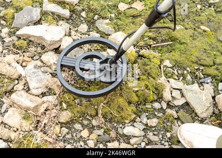 A man with a metal detector on the shore of a reservoir. Metal searches in the coastal zone. Stock Photo