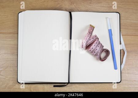 Blank notebook for records, pink tailor's tape measure and blue pen on a wooden table Stock Photo