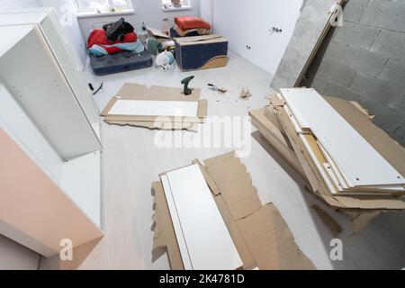 Parts of unfinished furniture, metal screws and tools lying on the floor with instruction manual for furniture assembly in the background. Moving to Stock Photo