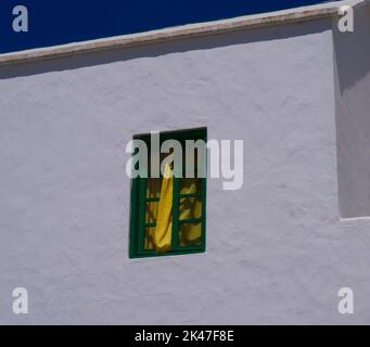 White house wall with green window and yellow curtain Stock Photo