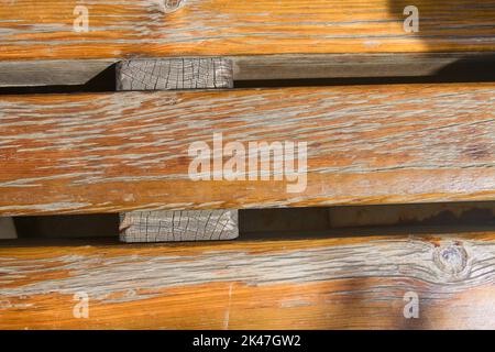 A public seat in the street formed by three natural woods with peeling paint form a rustic natural background Stock Photo