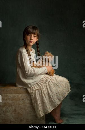 a girl with dark hair and two pigtails in a light dress sits with her legs tucked up and holds her favorite toy teddy bear in her hands Stock Photo