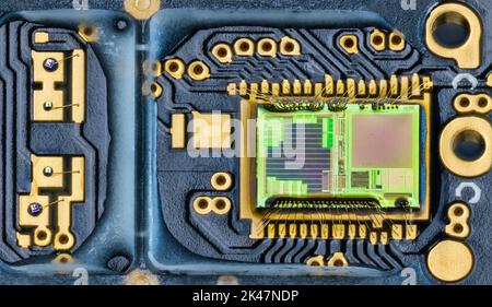 Closeup of green die inside integrated circuit of optical computer mouse. Electronic photodiode array, gold wires on blue PCB detail. Microelectronics. Stock Photo