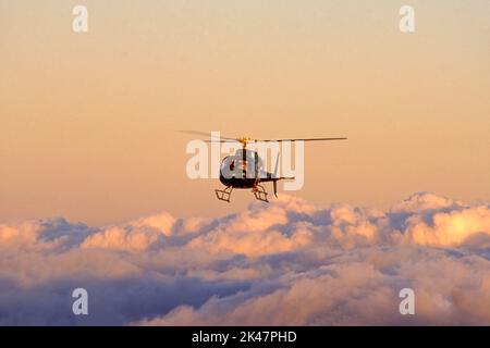 Helicopter flying over clouds at sunset. Stock Photo
