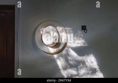 White hat hanging on the wall in the morning light. Minimalist modern interior Stock Photo
