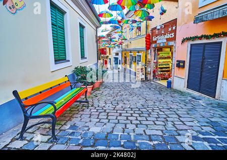 SZENTENDRE, HUNGARY - FEB 24, 2022: The rainbow bench and umbrellas over the narrow tourist street, on Feb 24 in Szentendre Stock Photo