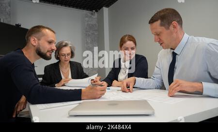 Four colleagues are discussing blueprints in a conference room in an office. Brainstorming of engineers and architects. Stock Photo