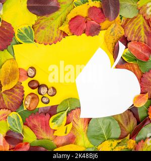 Creative layout made of dried leaves in autumn and paper card sticking out of the envelope with several chestnuts on the envelope. Flat lay concept. Stock Photo