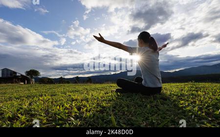 Woman praying for thank god praying with her hands together to think of a loving God, we praise God with light flare in the green nature. Stock Photo